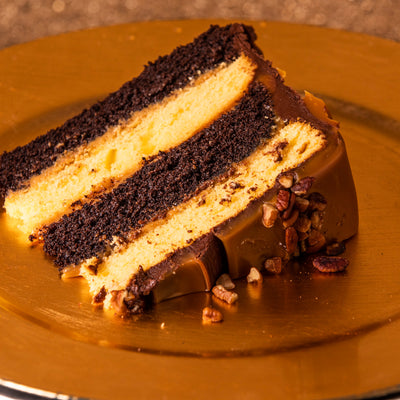 Slice of turtle cake with chocolate and yellow layers, caramel and pecans